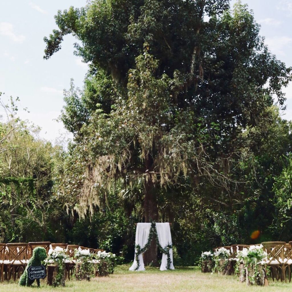 wooden arch and chairs set up for outdoor florida wedding ceremony under large oak trees